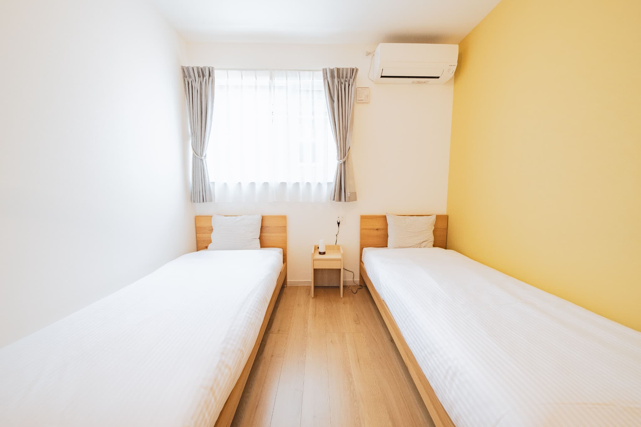 イエローのアクセントクロスが特徴のツインベッドルーム。明るくポップな印象で、シンプルな木製ベッドを配置。