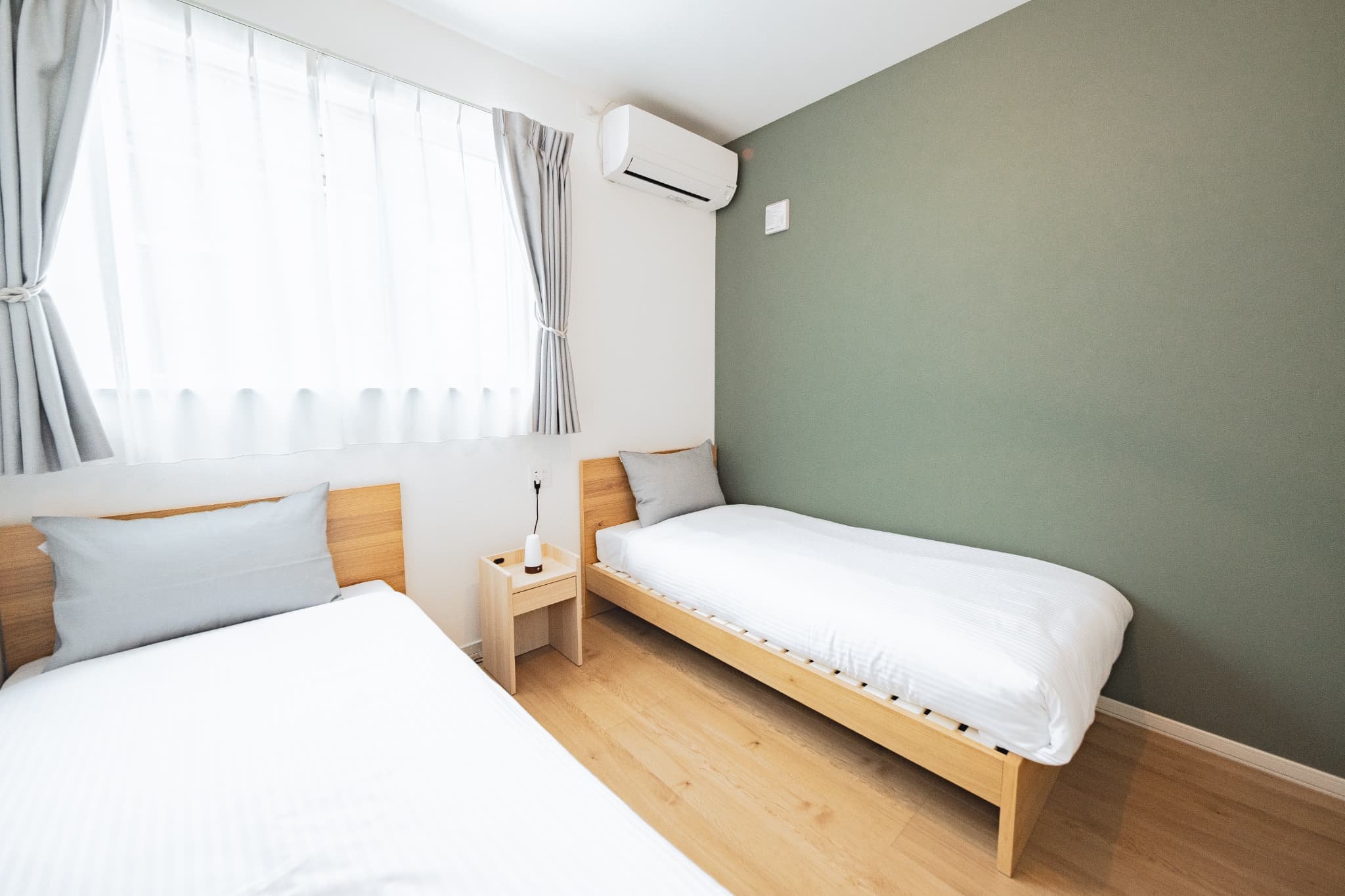 グリーンのアクセントクロスを採用したツインベッドルーム。木製ベッドと白い寝具で落ち着いた雰囲気を演出。