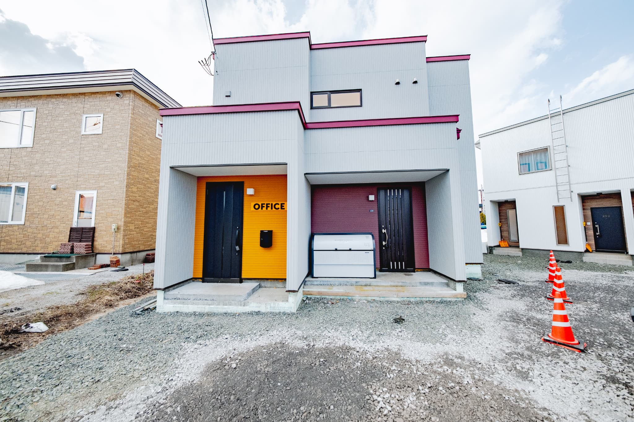 富良野市栄町に建つエゾムラサキA棟の外観。白壁にビビッドなカラーアクセントを組み合わせたモダンなデザインで、ゲストハウスとしての存在感を高めています。